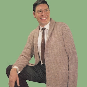 Puede incluir: Un cárdigan de punto beige con cuello chal y dos bolsillos. El cárdigan tiene cierre de botones y se lleva sobre una camisa blanca de botones con una corbata marrón.