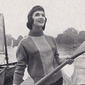 May include: A woman wearing a black and white patterned sweater with a turtleneck, holding a wooden oar. She is standing on a wooden dock with a boat in the background.