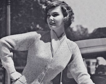 May include: A close-up of a woman wearing a light gray knitted cardigan with a V-neck and button closure. The cardigan has two pockets on the front and a subtle speckled pattern. The woman is standing next to a car and has her hand on the hood.