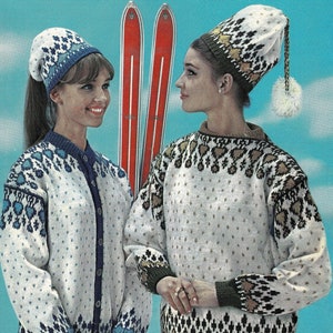 May include: Two women wearing white knit sweaters with colorful patterns and matching knit hats. The sweaters have a geometric design with blue, brown, and gold accents. The women are standing in front of a pair of red skis.