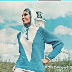 Pode incluir: Um suéter de malha com capuz em azul e branco, apresentando um painel frontal branco em forma de V, três botões azuis e padrões de flocos de neve. O modelo é intitulado Pullman wool, Sirdar 2015A, para bustos de 86, 91 e 97 cm.