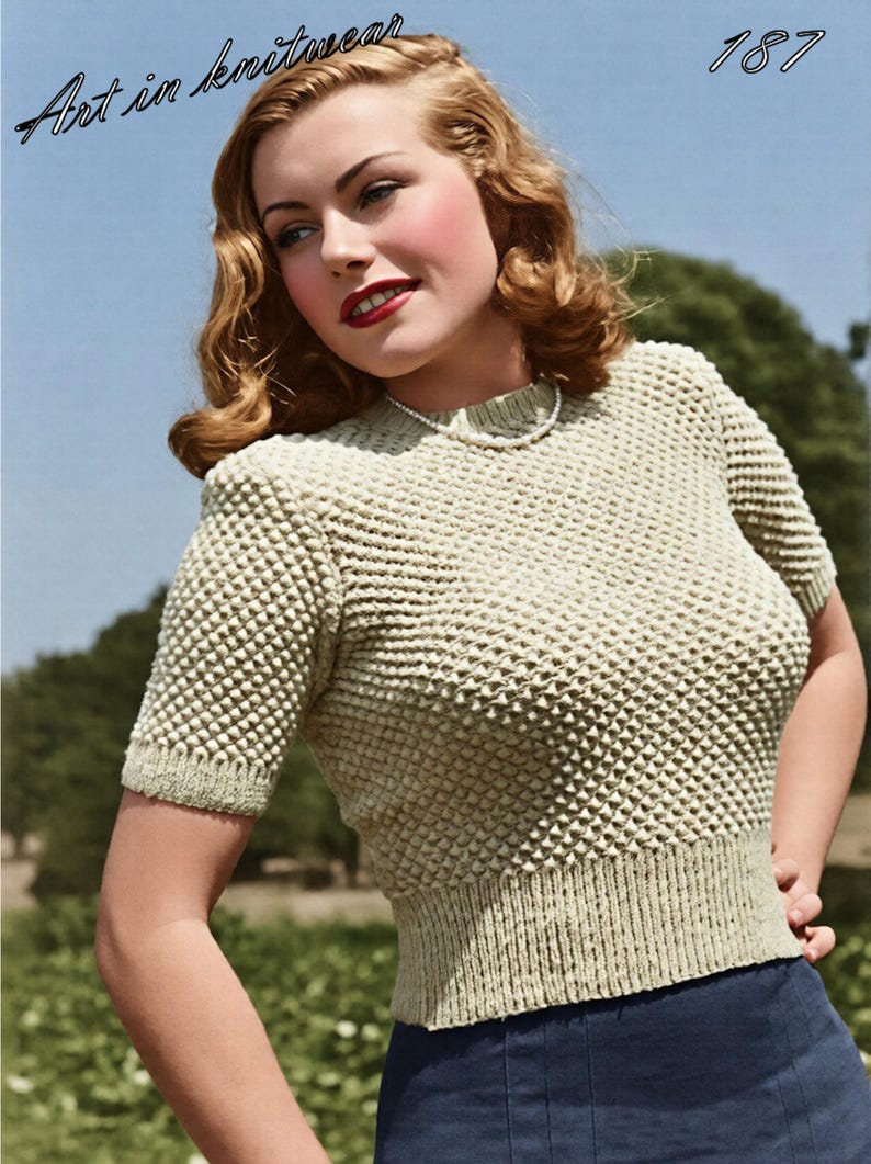 May include: A short-sleeved, light beige knit sweater featuring a textured, raised dot pattern throughout the body and sleeves. The garment has a ribbed crew neckline and a wide, ribbed waistband. The text "Art in knitwear" and "187" appear above.