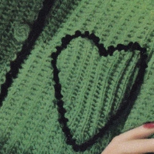 May include: A green knitted sweater with a black heart-shaped design. The sweater is made of a soft, textured yarn.