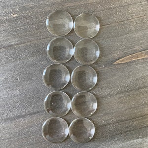 May include: Ten clear round glass cabochons, arranged in two rows of five, on a woodgrain surface.