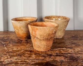 May include: Three terracotta pots of varying sizes, with a rustic, earthy brown glaze. The pots are arranged on a wooden surface.