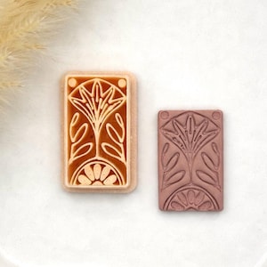 May include: Two rectangular stamps with floral designs. One stamp is light brown with a raised floral pattern, and the other is a darker reddish-brown with a similar design. The stamps are likely used for crafting or decorative purposes.