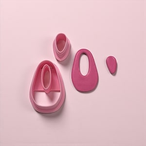 May include: A collection of pink polymer clay cutters in various teardrop shapes. The set includes a large teardrop, a smaller teardrop, and two nested oval shapes. The cutters are arranged on a light pink background.