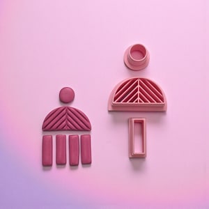 May include: Pink cookie cutters in various shapes, including a half-circle with a ribbed design, a circle, a rectangle, and a series of vertical rectangles. The cutters are arranged on a pink background.