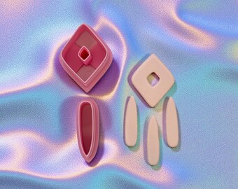 May include: Pink geometric-shaped cookie cutters. The set includes a diamond-shaped cutter with a smaller diamond cutout, a diamond-shaped cutter with a hole, and three teardrop-shaped cutters. The cutters are arranged on a holographic background.