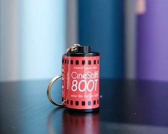 May include: A red and white film canister keychain with the text "CineStill 800T color film for low light" printed on it.