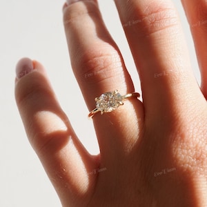 May include: A gold ring with a large oval-shaped diamond set in a prong setting. The ring is on a person's finger.