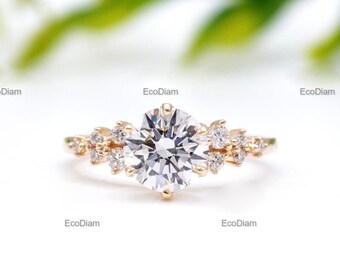 May include: A gold ring with a large, round, clear center stone and smaller accent stones. The ring has a floral design with multiple small stones clustered around the main stone. The ring is set against a soft, blurred background.