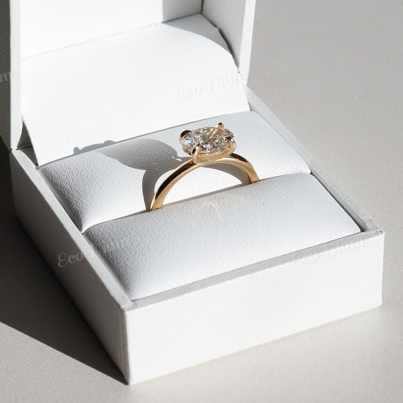 May include: A gold engagement ring with a large, clear diamond in a white ring box.