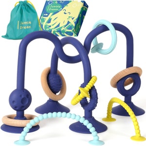May include: A set of blue, yellow, and brown silicone baby teethers with suction cups. The teethers are shaped like rings, arches, and spirals. The set comes with a blue drawstring bag with the words "Jumble Dream" printed on it.