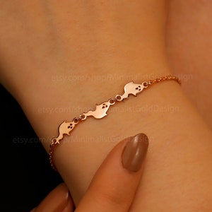 Op de afbeelding: Een delicate roségouden armband met een reeks gestileerde visbedels. De armband wordt om een pols gedragen en toont de fijne ketting en het herhaalde visontwerp. De sieraden zijn elegant en minimalistisch.