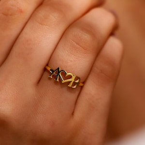 May include: A gold ring with the letters A and B on either side of a heart.