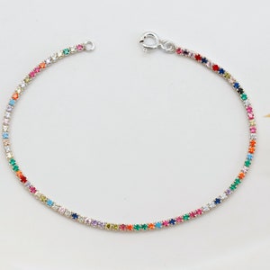 Pode incluir: Uma pulseira de prata com um arco-íris de pedras preciosas coloridas. A pulseira é feita de uma corrente fina e tem um fecho de lagosta.