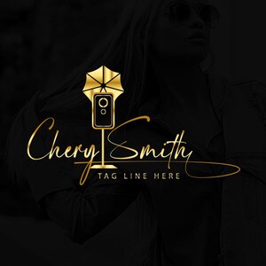 Puede incluir: Diseño de logotipo dorado con el nombre "Cheryl Smith" en escritura elegante. El logotipo incluye un icono de cámara estilizado con una parte superior en forma de paraguas. El lema "TAG LINE HERE" está debajo del nombre, sobre un fondo oscuro.