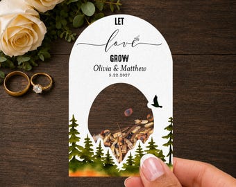 May include: A white arched seed packet favor with a circular cutout filled with seeds. The text reads LET love GROW, Olivia & Matthew, and 5.22.2027. The design features a watercolor forest of green pine trees and a small black bird silhouette.