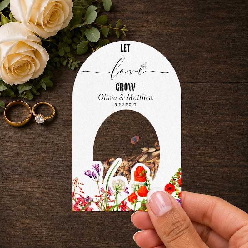 May include: An arched white paper seed packet featuring the text LET love GROW, Olivia & Matthew, and 5.22.2027. The design includes a central cutout revealing seeds and a colorful floral illustration with red, purple, and green botanical elements.