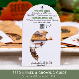May include: A white arched seed packet containing a wildflower seed mix. The front features text including Wildflower Seed Mix, Non GMO, Open Pollinated, Untreated, and a QR code for a growing guide. The packet has a crescent-shaped clear window.