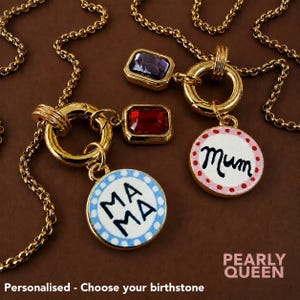May include: Two gold-toned necklaces featuring circular pendants with white centres and blue or pink polka-dot borders. The blue pendant reads MAMA and the pink reads MUM. Each necklace includes a rectangular birthstone charm and a gold chain.