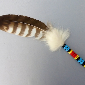 May include: A brown and white striped feather with a white fluffy tip. The feather is adorned with colorful beads in red, yellow, blue, and black.