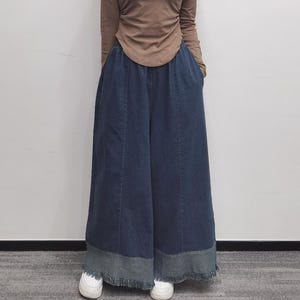 May include: Wide-leg denim pants with a frayed hem and a dark blue wash. The pants have a relaxed fit and are made of a soft, comfortable fabric.