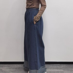 May include: A long, dark blue denim skirt with a wide waistband. The skirt has a relaxed fit and falls to the ankles.