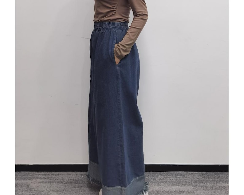 May include: A long, dark blue denim skirt with a wide waistband. The skirt has a relaxed fit and falls to the ankles.