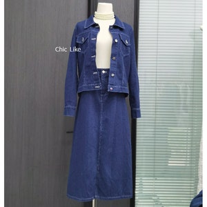 May include: A denim jacket and skirt set in a dark blue shade. The jacket has a classic collar, button closure, and two front pockets. The skirt is A-line and falls to the knee.