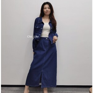 May include: A denim jacket and skirt set in a dark blue shade. The jacket has a classic collar and button closure. The skirt is A-line and has a front slit.