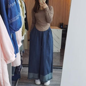 May include: A woman wearing a brown long-sleeved shirt and blue denim wide-leg pants with a frayed hem.