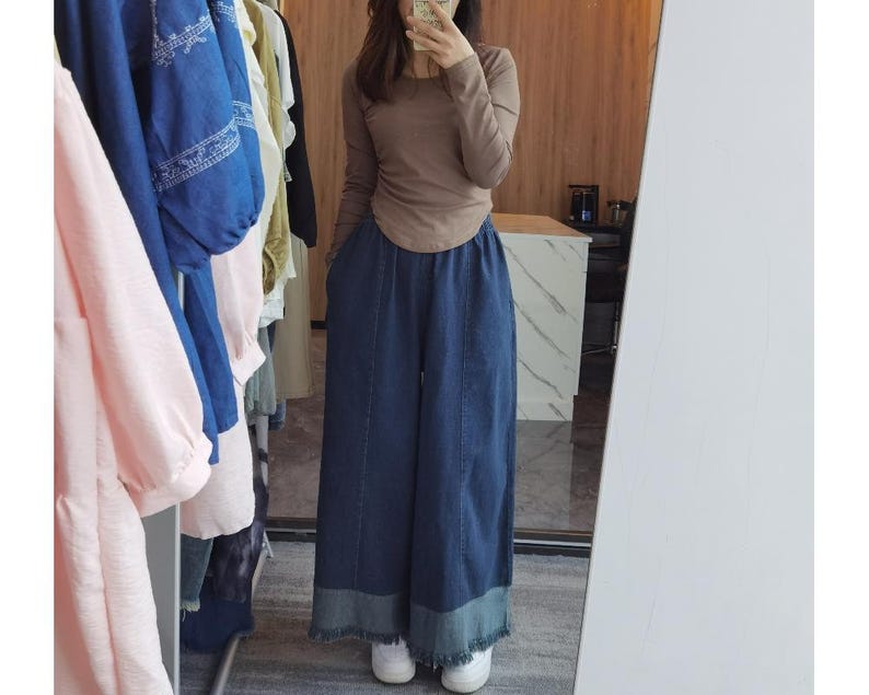 May include: A woman wearing a brown long-sleeved shirt and blue denim wide-leg pants with a frayed hem.