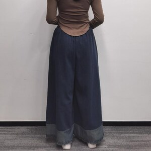 May include: Wide-leg denim pants with a frayed hem. The pants are a dark blue color and have a relaxed fit.