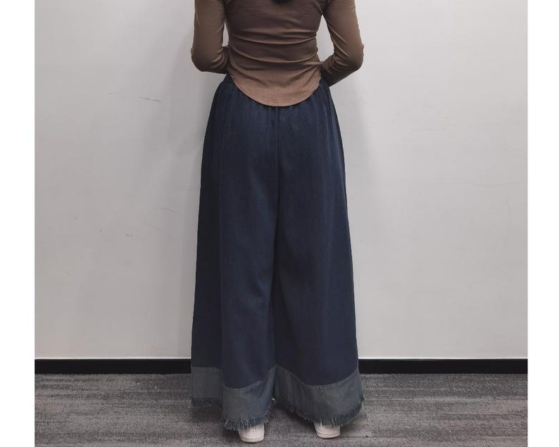 May include: Wide-leg denim pants with a frayed hem. The pants are a dark blue color and have a relaxed fit.