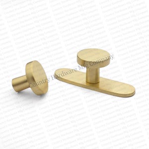 May include: Gold-toned cabinet hardware set, including a knob and a pull with a rounded top. The hardware has a smooth, matte finish. The knob is cylindrical with a flat top. The pull is rectangular with a rounded top.