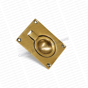 May include: A brass-toned recessed pull with a circular handle and a rectangular backplate. The hardware has a classic design with four screw holes in each corner. The product is likely for cabinetry or furniture.