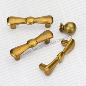 May include: Three brass cabinet knobs with a bowtie design. The knobs are in various sizes and shapes. The knobs are on a white background with the text "Country Hardware Mfg Company" repeated.