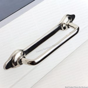 May include: A polished nickel cabinet pull with a smooth, curved handle and two teardrop-shaped mounting plates. The hardware features a reflective metallic finish and is mounted on a white surface with the text Country Hardware Mfg Company.