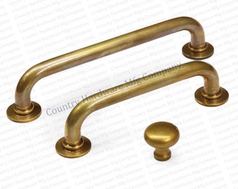May include: Two brass cabinet pulls and a knob. The pulls are curved with rounded ends and circular bases. The knob is a small, rounded dome shape. All pieces have a warm, golden finish, suggesting a vintage or antique style. Hardware for furniture.