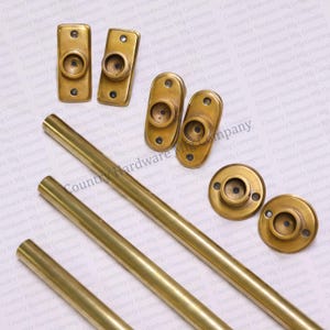 May include: Four gold-toned metal curtain rods and six gold-toned metal finials. The finials have a round shape with a small hole in the center. The rods are smooth and have a shiny finish.