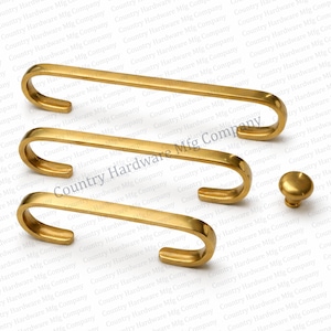 May include: A set of gold-colored cabinet hardware, including three pull handles and a round knob. The handles have a curved design, and the knob is a simple, rounded shape. The hardware is likely made of brass or a similar metal.