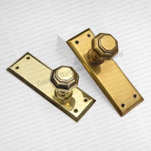 May include: Two antique brass door handle sets. Each set includes a rectangular backplate and an octagonal knob. The text "Country Hardware" is visible on the knob. These vintage door hardware pieces are likely for restoration projects.