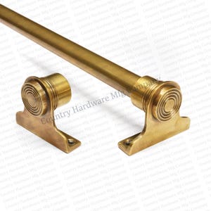May include: A brass-colored curtain rod with decorative end pieces. The rod is cylindrical, and the end pieces have a spiral design. The hardware is designed for mounting to a wall. The image is of a new product.
