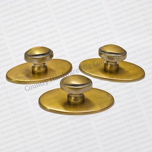 May include: Three brass cabinet knobs, each featuring a rounded top and a short, cylindrical stem attached to a smooth, flat, oval-shaped base plate. The metal has a warm, polished finish with subtle variations in tone across the surfaces.
