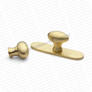 May include: A set of brass door hardware, including a knob and a backplate with an oval-shaped knob. The hardware has a polished finish and is designed for door installation. The set is new and unused.