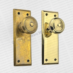 May include: Two antique brass door knobs with square backplates. The knobs have a round, raised design.