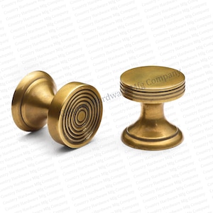 May include: Two antique brass cabinet knobs. One knob features a spiral design, while the other has a flat, ridged top. The knobs have a warm, golden hue and are likely made of solid brass.