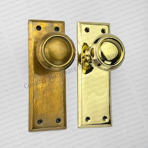 May include: Two antique brass door knobs with square backplates. The knobs have a rounded, domed shape with a raised rim.